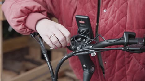 Frau-Mit-Roter-Jacke,-Die-Den-Lenker-Eines-Elektrofahrrads-Justiert,-Das-Sie-Gerade-Gekauft-Hat