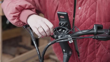 mujer con una chaqueta roja ajustando el manillar de una bicicleta eléctrica que acaba de comprar