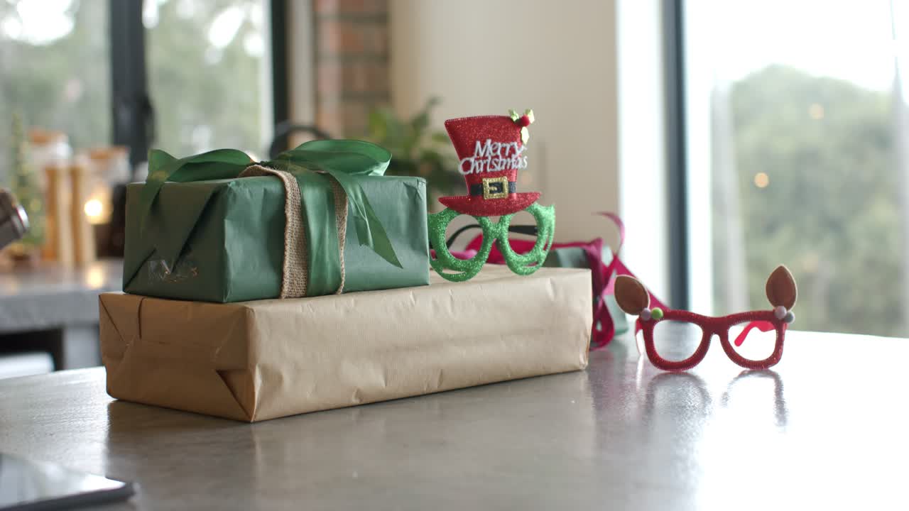 Die Aufnahme ist ruhig und zeigt einen Geschenke-Stapel mit Partybrillen am Fenster, durch das Blattwerk zu sehen ist