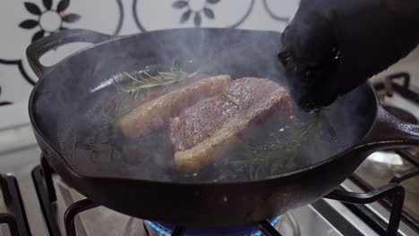 adding rosemary to grilled steak on hot pan