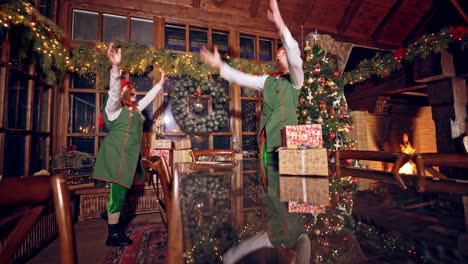 two elves are standing in specially decorated room near the table and throwing presents to each other. feast fireplace in the background. christmas spirit concept close up video. christmas eve. new year is coming. elves are putting presents on the table.