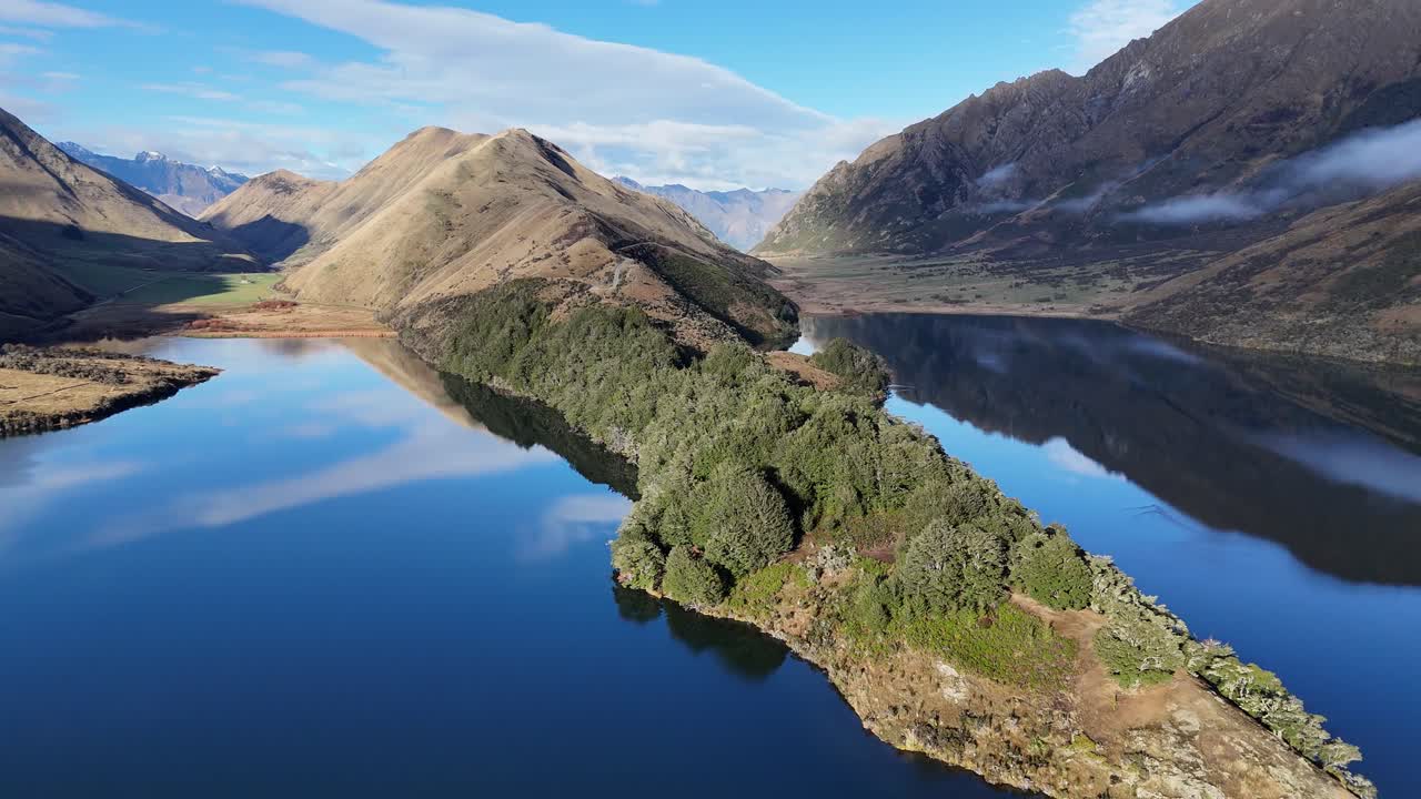 Drone footage captures Lake Moke's serene beauty with lush greenery and reflective waters under clear skies in Queenstown, New Zealand
