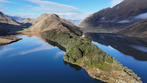 drone footage captures lake moke's serene beauty with lush greenery and reflective waters under clear skies in queenstown, new zealand