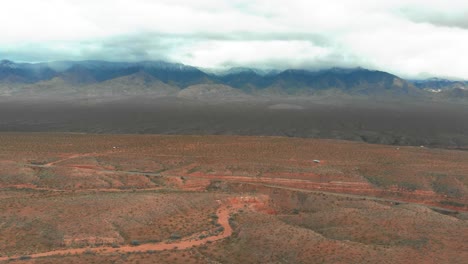 Aerial-shot-of-the-drylands-in-Utah-with-offroad-trails-and-the-rocky-mountains-in-the-background-on-a-cloudy-day