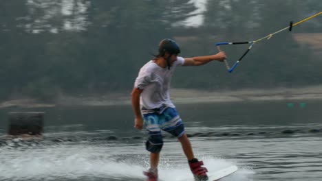 Side-view-of-caucasian-young-man-doing-tricks-on-wakeboard-in-the-city-lake-4k