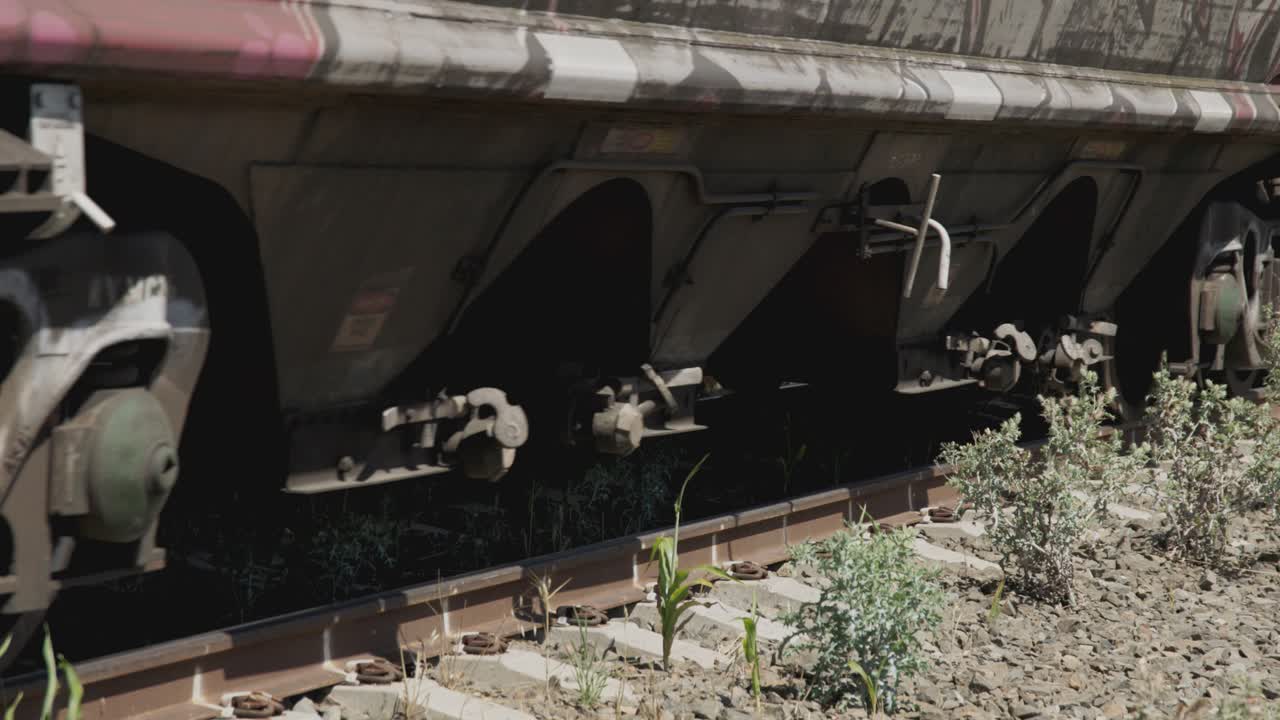 Close-up shot of the wheels and undercarriage of a graffitied freight train moving along a rural railway track.