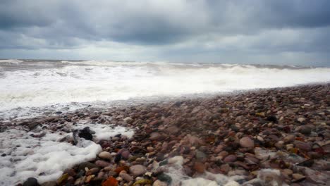 powerful stormy rolling coastal ocean waves foam blowing in rough windy weather on pebble shore