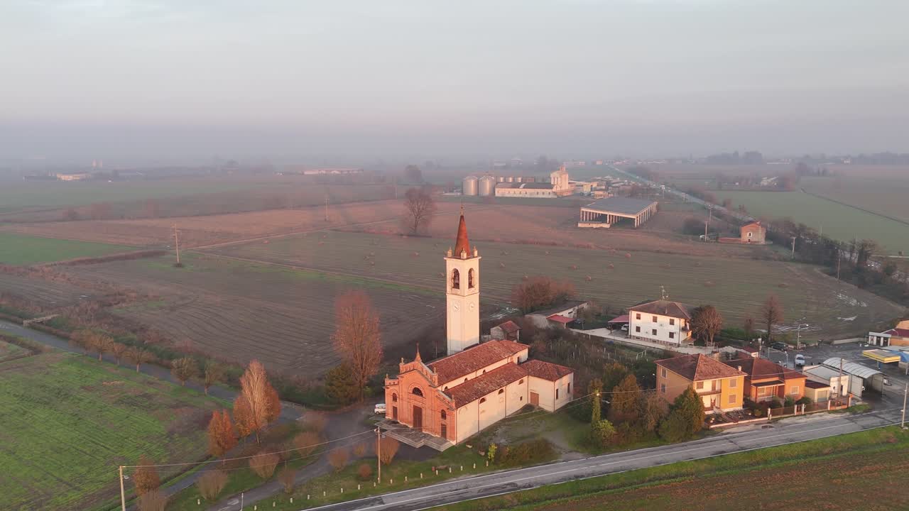 Paesaggio rurale italiano che mostra Strada Padana Inferior S.S.10 Via Mantova con auto di passaggio, vicino all'iconica Trattoria La Resca e alla chiesa di San Bartolomeo a Vescovato, Cremona, Italia