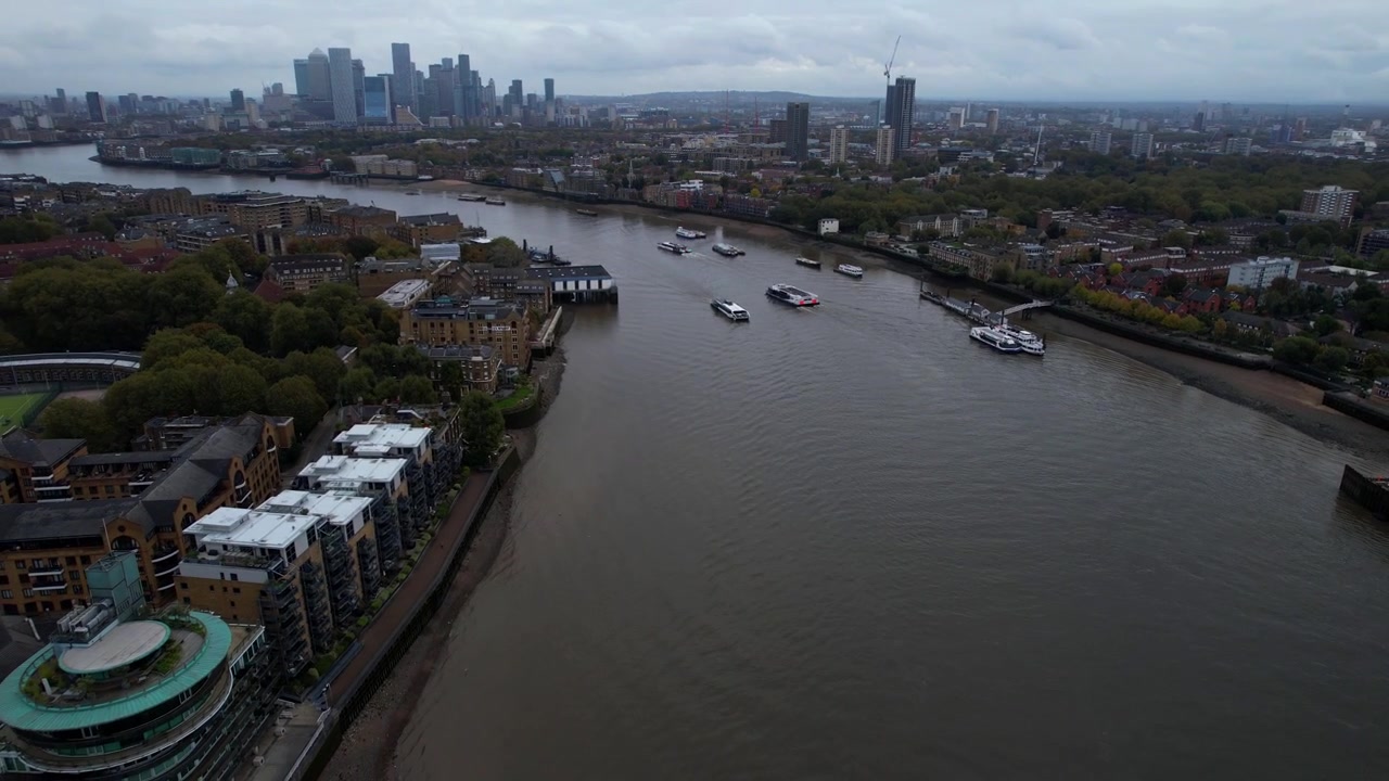 Aerial reveal of River Thames with boats navigating and Canary Wharf in background. London, UK