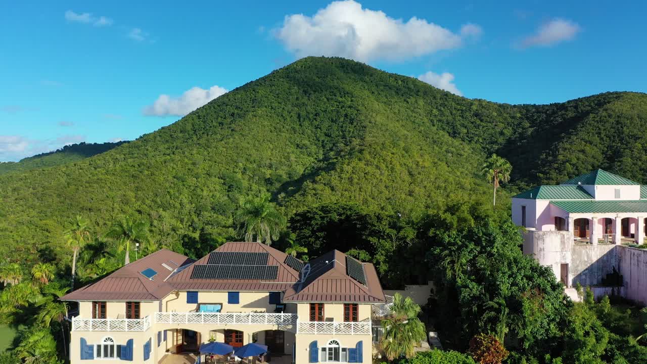 This drone view above St. Croix features a few private villas hidden in dense trees, perched along forested hills with sloping terrain and hazy green mountains completing the tropical island scene