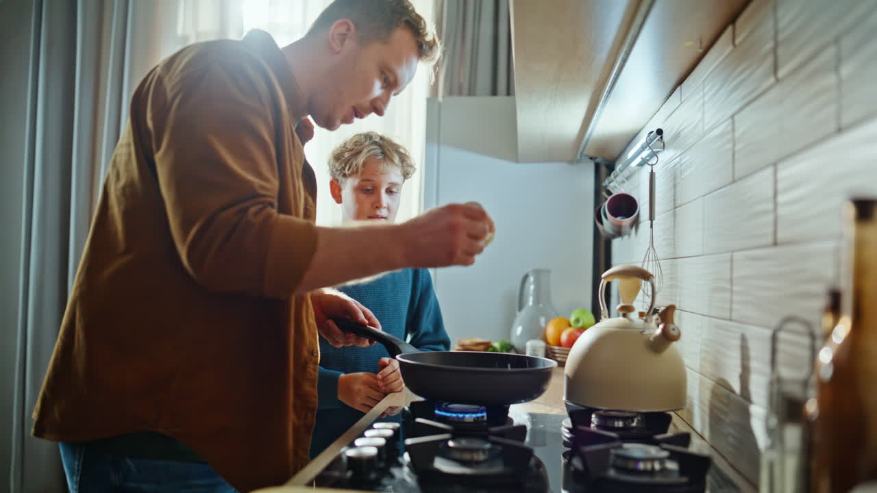 Sohn hilft Vater beim Braten eines Frühstücksomeletts am Küchenherd, Nahaufnahme. Fürsorglicher Mann