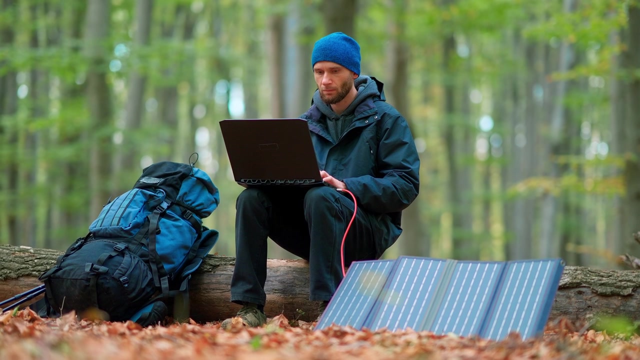 Man Working on Laptop in Forest, Charging with Portable Solar Panel