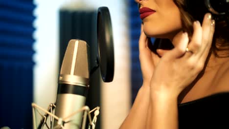 una hermosa mujer con auriculares graba una canción en un estudio de grabación profesional.