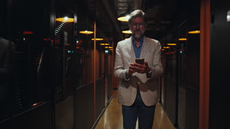 businessman using smartphone while walking through modern office hallway