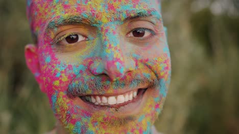 close-up portrait of cheerful mixed race guy with colorful face standing outside at holi party