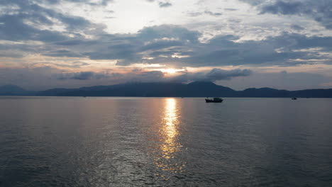 Beautiful-Vietnamese-landscape-of-golden-sunset-reflecting-over-ocean-with-mountains-and-traditional-fishing-boat