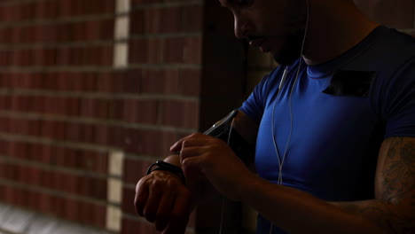 male runner at night checking fitness app on watch in street