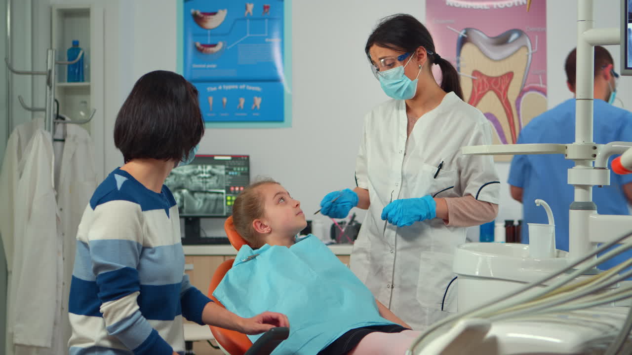 estomatologista pediátrico segurando ferramentas estomáticas falando com a mãe da criança