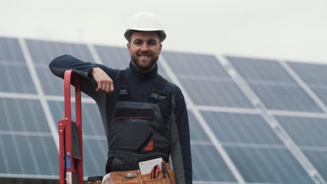 portrait of a young man in a work uniform with a toolbox in his hands on the background of a solar power plant