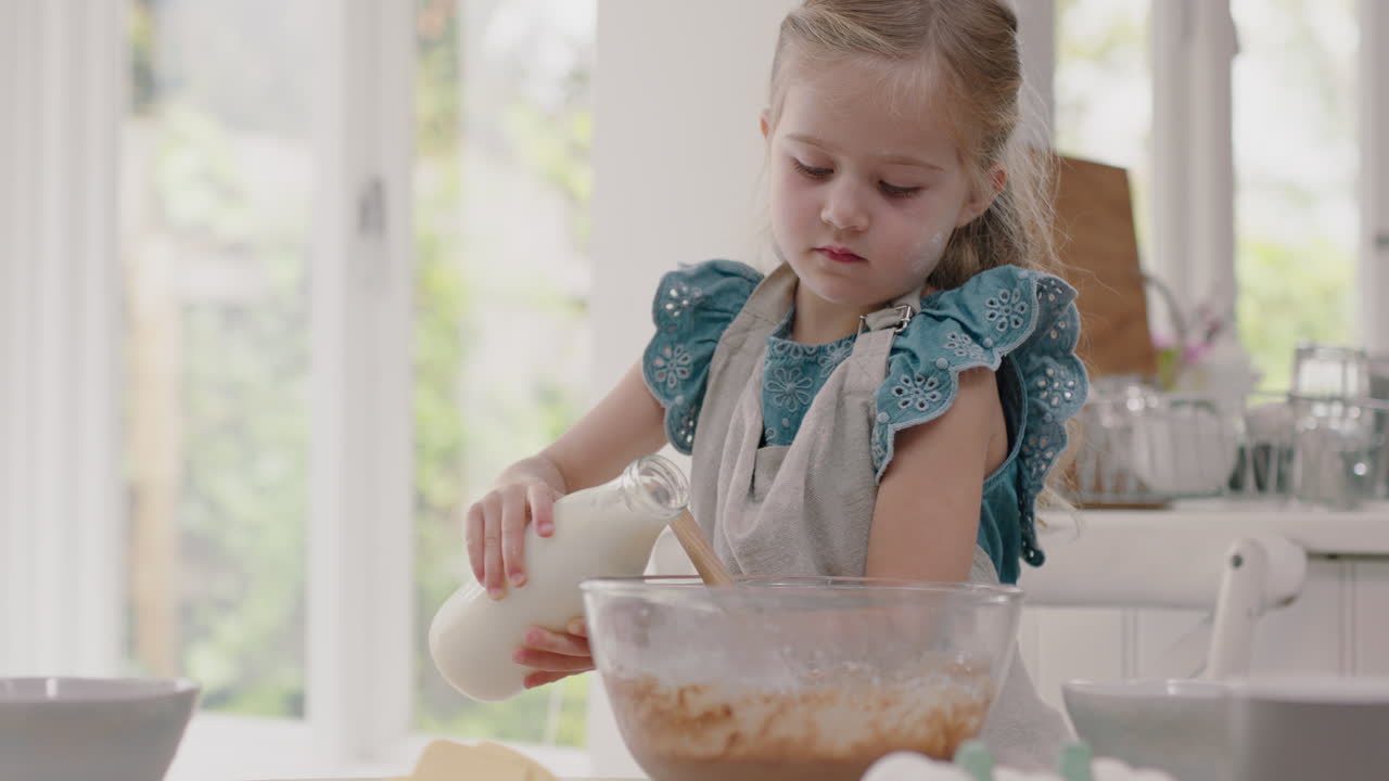 niña feliz horneando en la cocina mezclando ingredientes para masa de galletas casera vertiendo leche en el cuenco divirtiéndose preparando deliciosas golosinas para el desayuno en casa 4k metraje