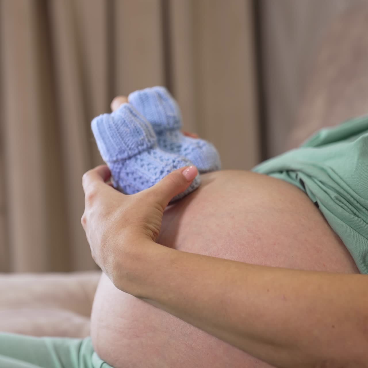 Il pancione di una donna incinta. Futura mamma che tiene in mano dei calzini di lana sul ventre. Primo piano. Vista laterale