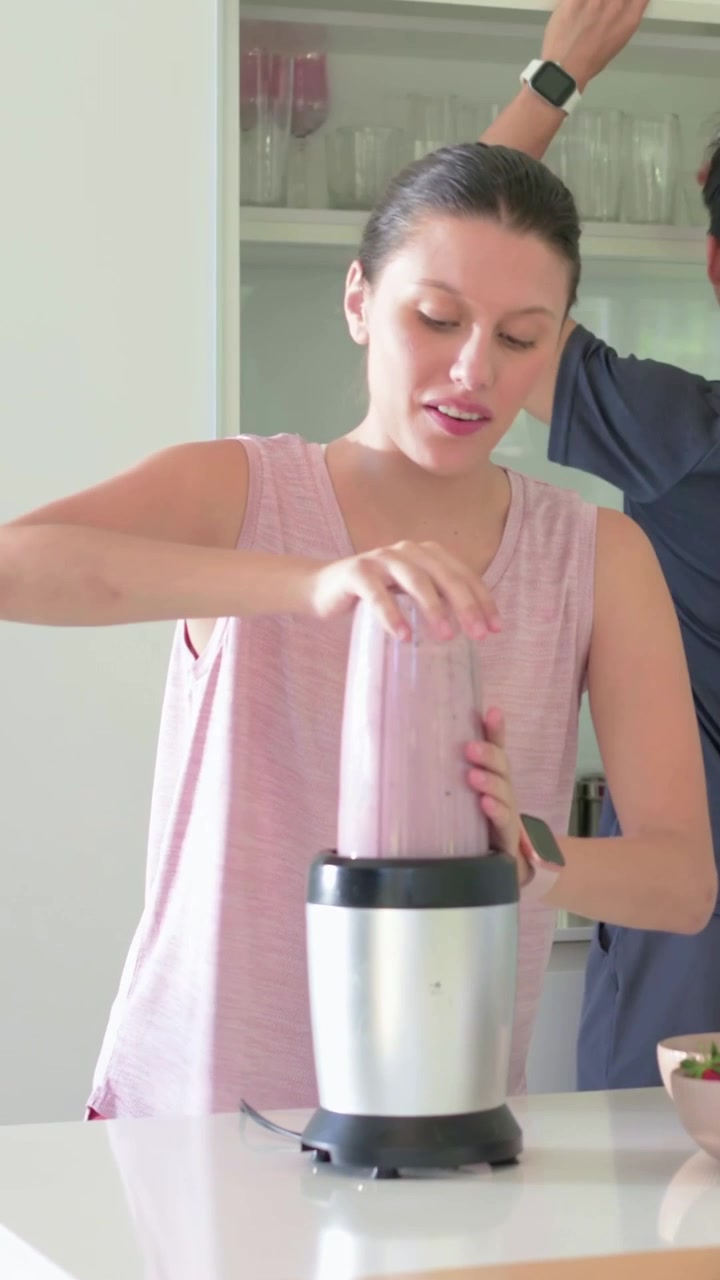 Video verticale: Donna che posiziona la base, indossando una canotta rosa, mentre fissa un barattolo, miscela, tappa e prepara per l'asporto al bancone.