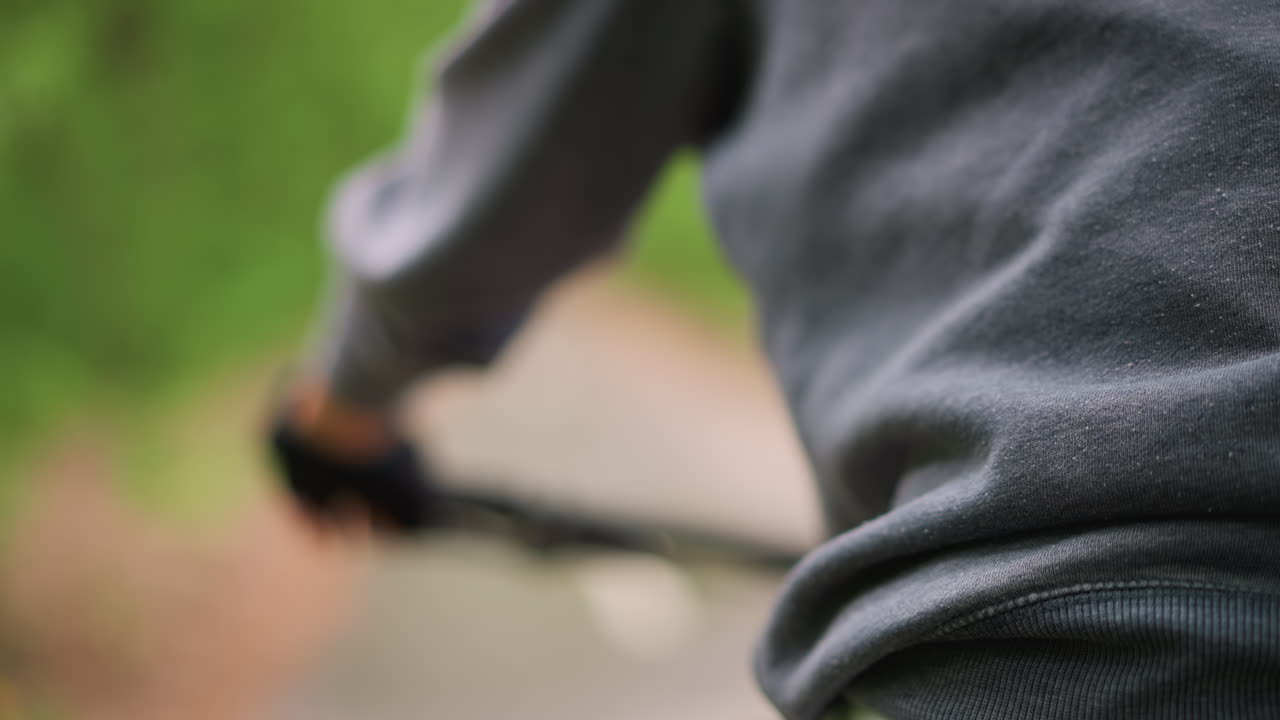 Handlebar Grip And Forearm In Motion, White Woman Wearing Hoodie And Gloves Steers Along Leafy Path, Visible Brake Cable And Textured Rubber, Intimate Control Shot For Action And Lifestyle Projects
