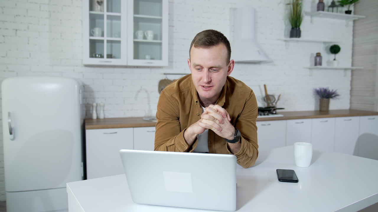Young businessman having a video conversation at home. Student speaking in front of a wireless laptop on kitchen background. Remote job.