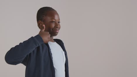 Studio-Portrait-Of-Boy-Smiling-And-Giving-Thumb-Up-Gesture-Against-White-Background