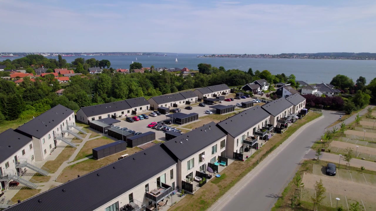 Luftoptagelse af et moderne boligkvarter beliggende ud til en rolig kystkulisse.