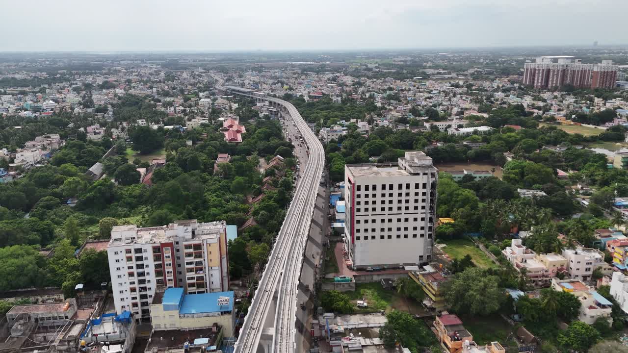 Vista aerea del sobborgo di Kattupakkam a Chennai, che mostra la complessa costruzione della Fase 2 della metropolitana e una nuova strada sopraelevata che passa sopra una fitta distesa residenziale, evidenziando lo sviluppo urbano