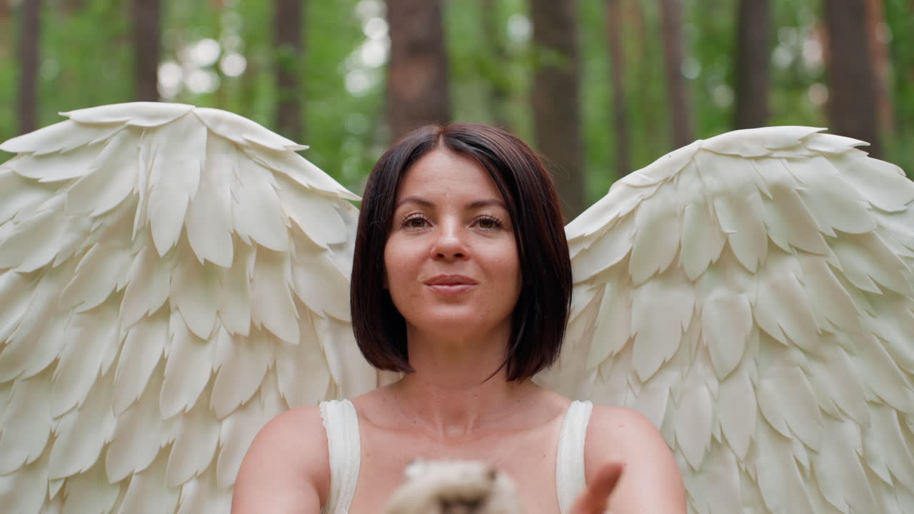 Winged woman portrayed as beloved of Eros holds carved staff and casts spell with serene expression, surrounded by lush green forest, exuding magical warmth and divine energy