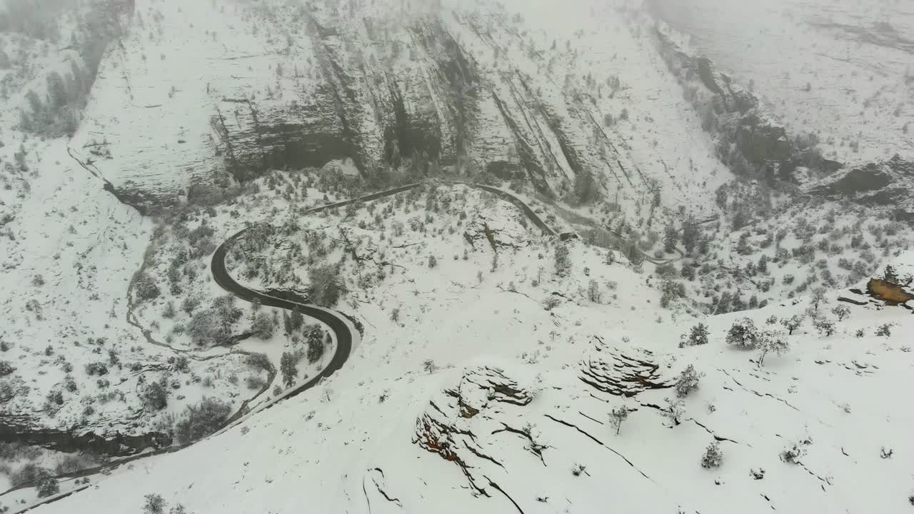 Stunning Aerial pan up shot of some snow covered trees then revealing a road separating two mountain ridge lines covered in fog.