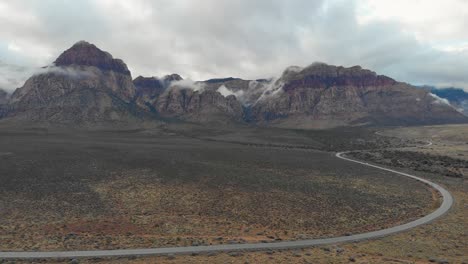 Aerial-drone-shot-of-an-empty-road-highway-with-mountains-and-low-clouds-in-the-background