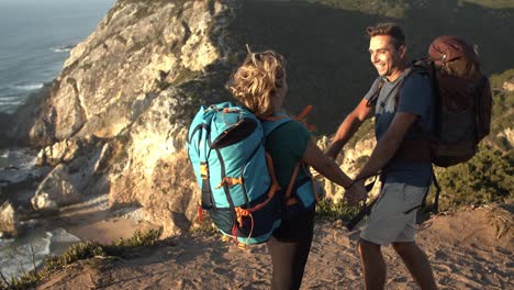 Couple-of-excited-backpackers-standing-at-cliff