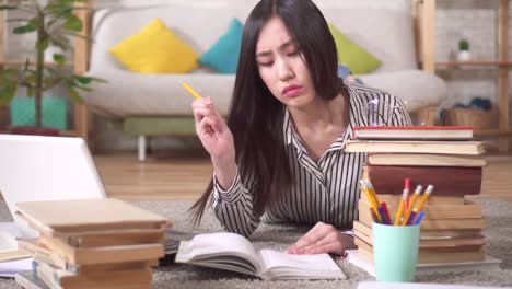 tired asian student is preparing for the exam lying on the floor in the living room with a laptop and books