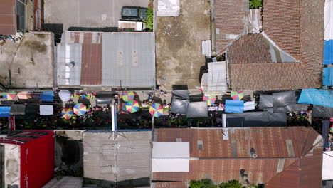 Top-down-aerial-that-is-slowly-lowering-revealing-the-market-on-the-street-below-in-between-the-buildings-in-San-Juan-Ostuncaclo,-Guatemala