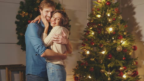 una pareja abrazándose junto al árbol de navidad.