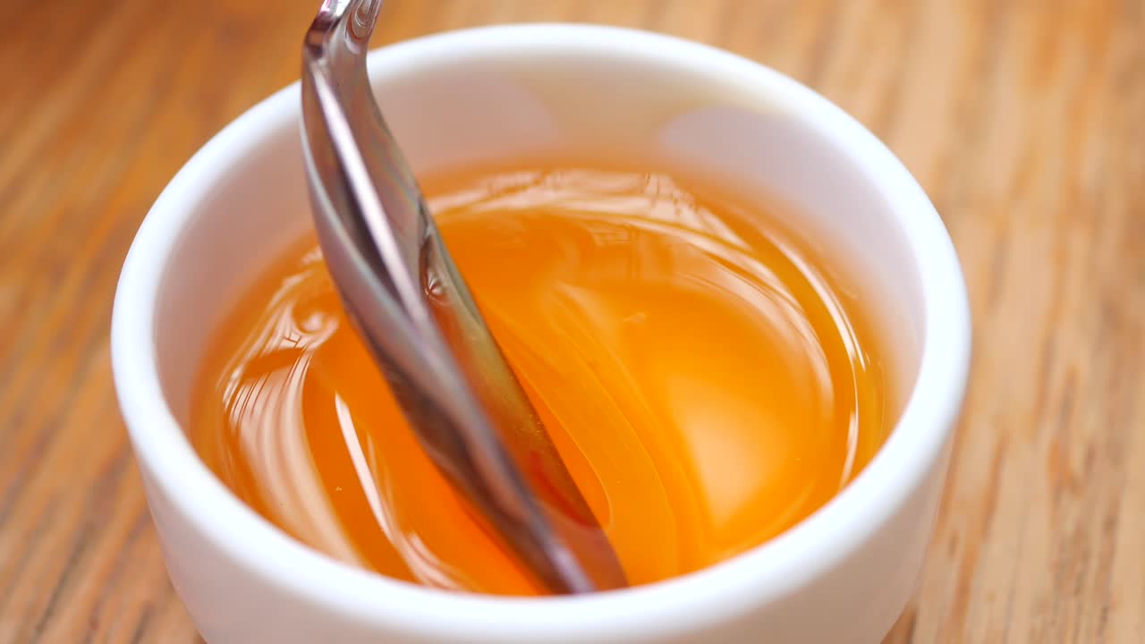 A close up of a spoon dipping into a bowl of honey