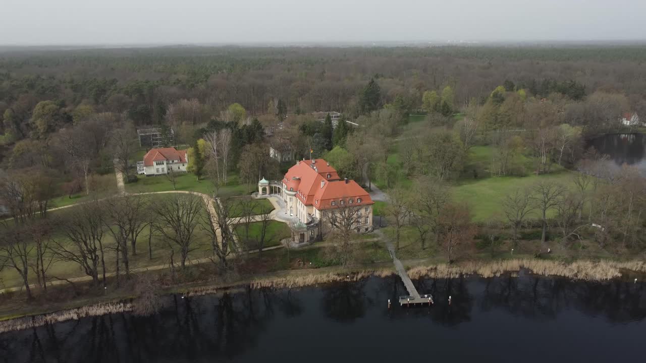 Aerial view of a large, secluded German house surrounded by a peaceful lake, showcasing serene nature and European countryside charm.
