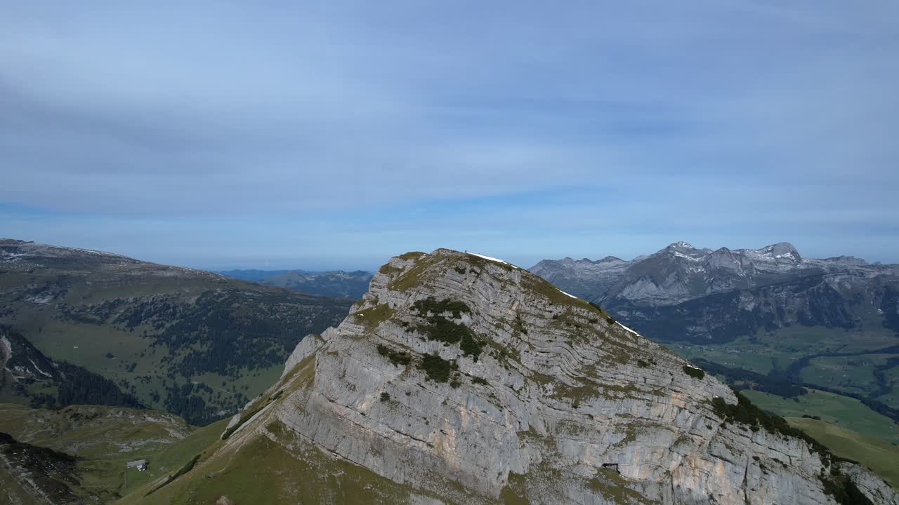 Aerial backwards shot of Margelchopf Mountain in Switzerland at cloudy day. Wide shot panorama with green mountains and valley at summer season. dolly backwards.