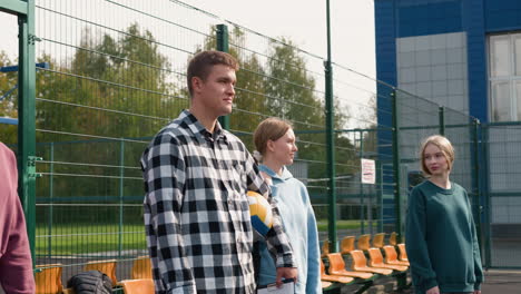 young athletes and their coach, clad in athletic wear and carrying bags, standing in a volleyball court with lush trees in the background, poised for a session