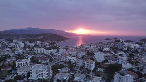 Carretilla-Aérea-Sobre-La-Riviera-De-Ksamil-Con-Vistas-A-La-Impresionante-Puesta-De-Sol-Naranja-En-El-Horizonte