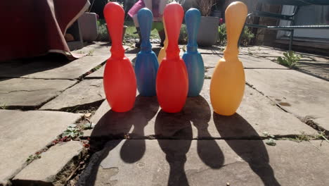 chica vestida de rosa jugando con bolos de juguete en el jardín, en un brillante día de primavera