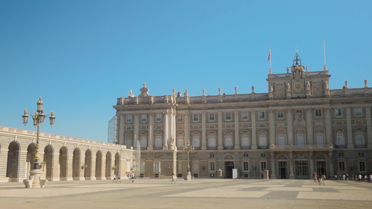 Un'ampia inquadratura dello storico Palazzo Reale di Madrid, caratterizzato da un'architettura in pietra ornata e dal grande cortile sotto un cielo estivo luminoso. Utile per documentari di viaggio e storia europea.