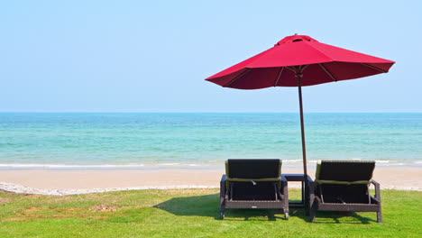 couple of empty beach beds under red parasol on majestic tropical beach on sunny day, caribbean holiday scenery, full frame