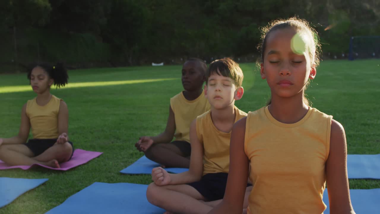 grupo diverso de escolares sentados en esteras meditando durante una lección de yoga al aire libre