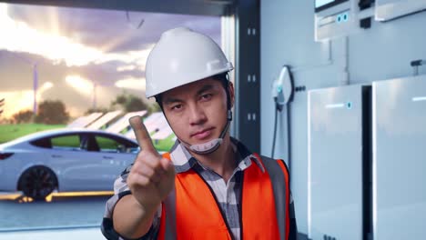 close up of asian male engineer with safety helmet disapproving with no index finger sign while standing with home energy storage system in a modern garage