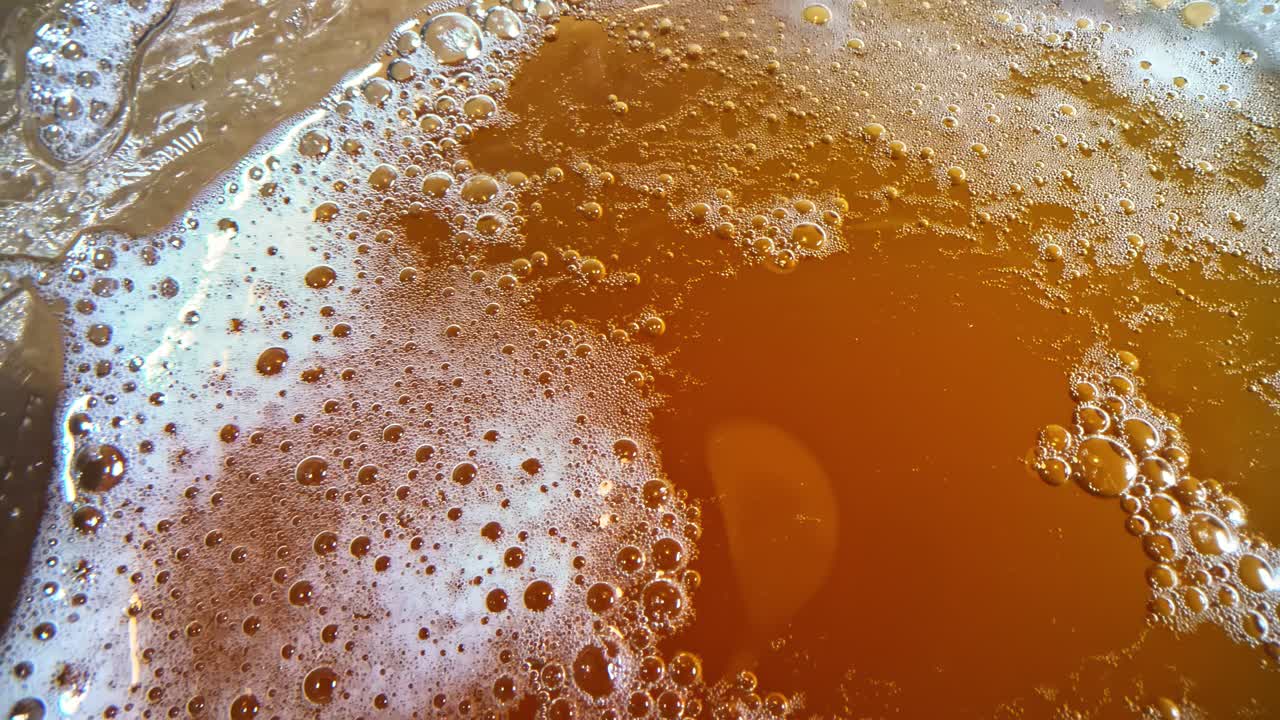 Extreme close-up panning over a glass of golden cider, showing bubbles, foam, and light reflections across the surface of the sparkling drink