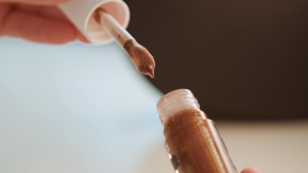 Close view of hands removing white dropper cap from amber glass bottle and gently dispensing shimmery liquid bead into bottle mouth, showing twisting, lifting, and dripping motion, with hand, dropper